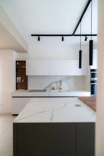 Cucina moderna con mobili bianchi, ripiani in marmo e paraschizzi. Un rubinetto nero è al centro dell'isola. Luci pendenti nere e luci a binario eleganti pendono dal soffitto, conferendo un tocco contemporaneo. Ipogeo Architetti