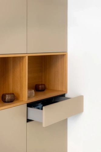 Mobile contenitore beige minimalista con ripiani in legno aperti e un cassetto parzialmente aperto. Piccole pietre decorative sono posizionate sui ripiani. Il design presenta linee pulite e un'estetica moderna. Ipogeo Architetti